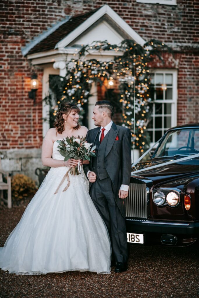 A married couple stand in front of a vintage Rollsroyce
