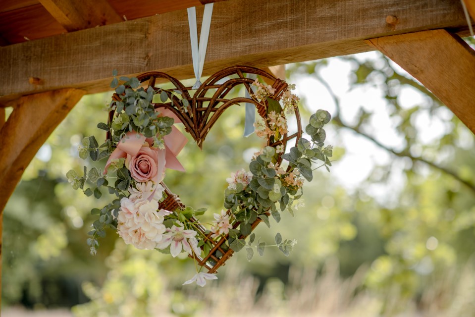 Wicker heart with flowers hanging from an oak beam outside