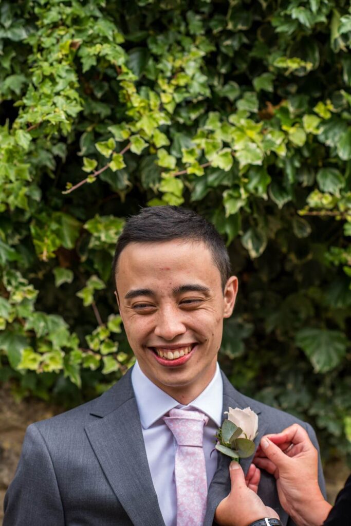 A pink buttonhole is attached to the grooms suit ready for the tiny wedding at the Castle Westenhanger, Kent, England
