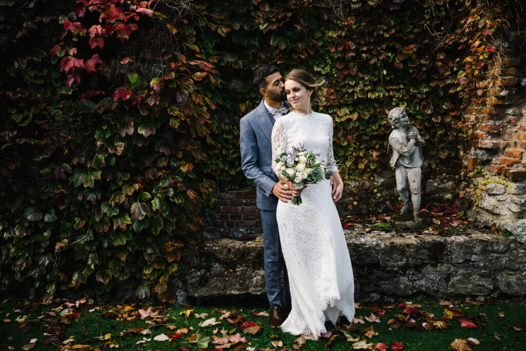 The couple enjoy moments with their elopement photographer outside the Castle Westenhanger in Kent England amongst the autumn leaves.