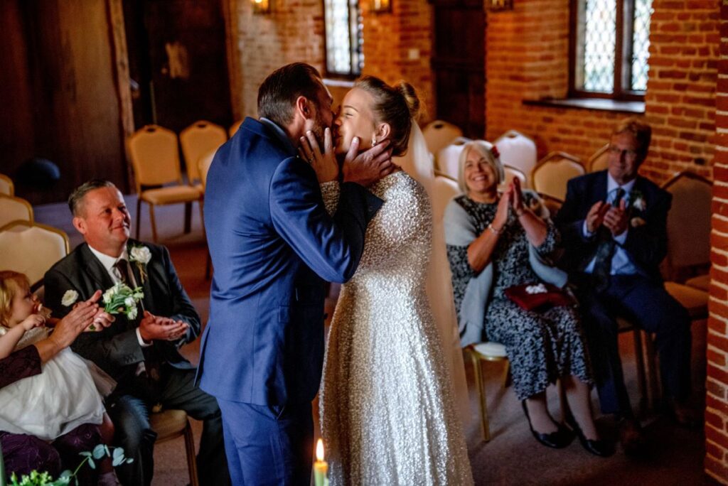 The bride and groom kiss each other after saying I do in the Queen Elizabeth ceremony room in the fortified 14th Century manor house in Kent