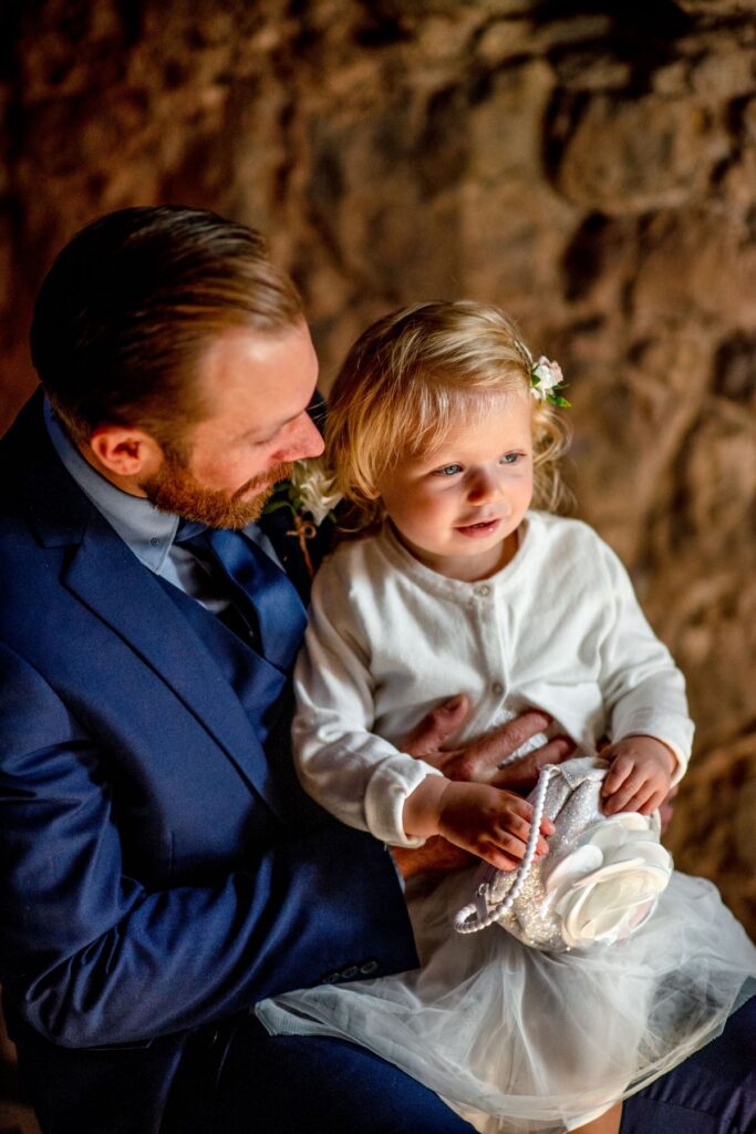 A groom dressed in a blue suit with his baby girl just before saying I do at the Castle Westenhanger in Kent