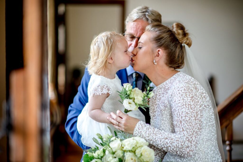 A bride in a pearl wedding dress kisses her baby girl on the lips just before marrying at the Castle Westenhanger, Kent in an intimate ceremony
