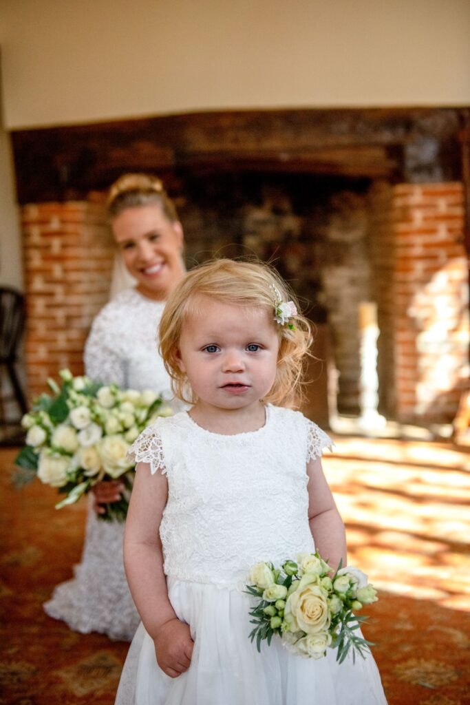 A bride in a pearl wedding enjoys watching her little girl fasinated with the photographer just before marrying at the Castle Westenhanger, Kent in an intimate ceremony