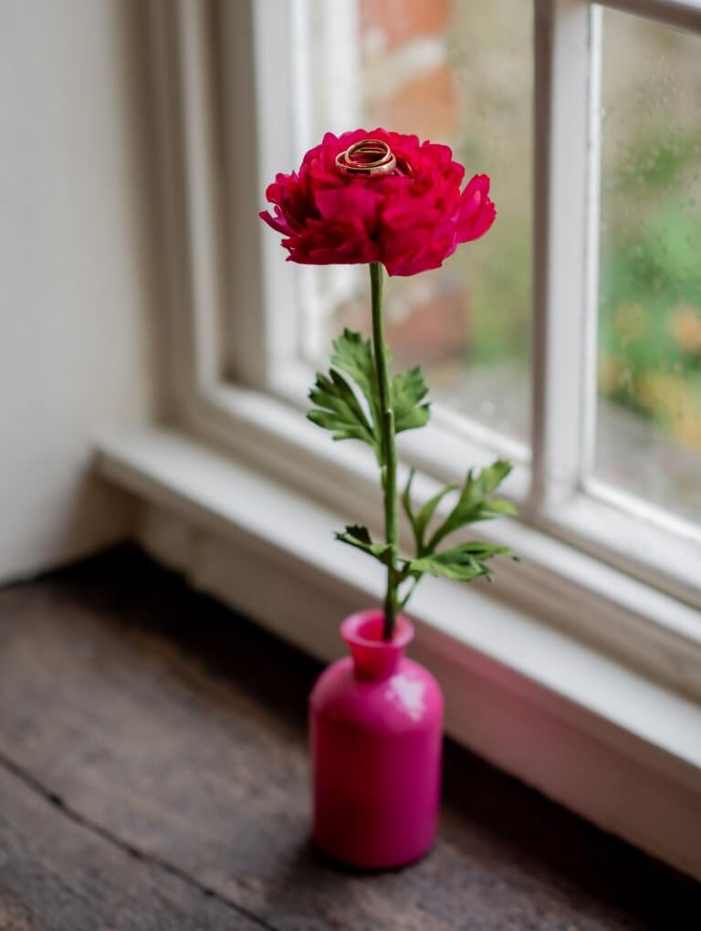 Wedding bands are perched onto of a pink flower in a pink vase during an elopement at the Castle Westenhanger