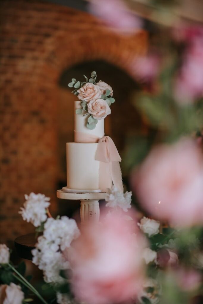 A two-tier elopement wedding cake with pink sugar iced slowers and a silk ribbon at the Castle Westenhanger hanger