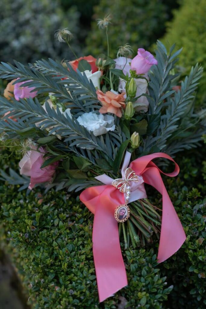A spring bouquet tied with a pink satin ribbon, and decorated with a memory pin, laid ontop of a hedge at Allington Castle, Maidstone, Kent, England