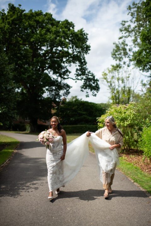 An eloping Bride photographed walking on the Bilsington Priory estate with Ruth of House of Mimi Fleur picking up her dress, near Ashford, Kent, England